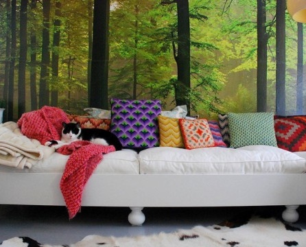 Sofa putih dengan bantal berwarna-warni di bawah kertas dinding landskap